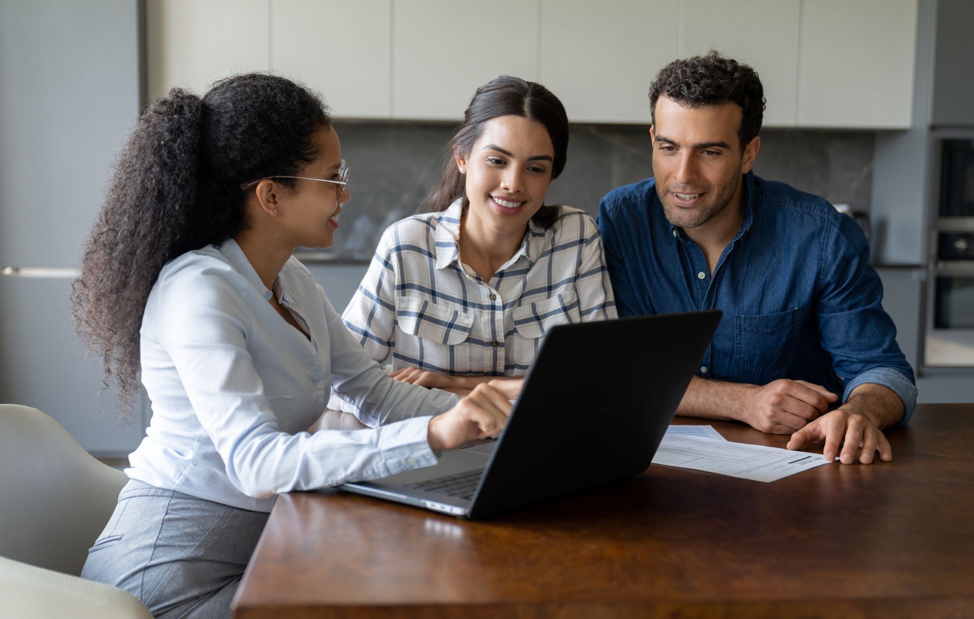A man and a woman are sitting at a table looking at a laptop computer.