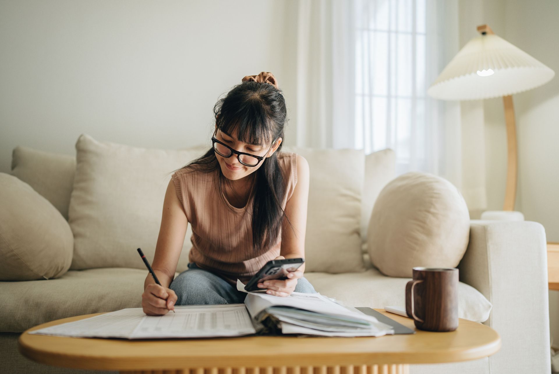 A woman is sitting on a couch writing on a piece of paper.