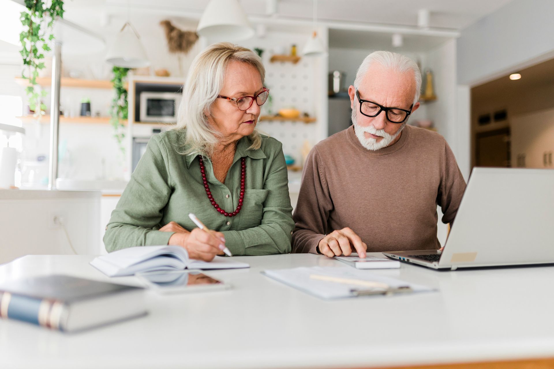 An elderly couple is sitting at a table looking at a laptop computer.
