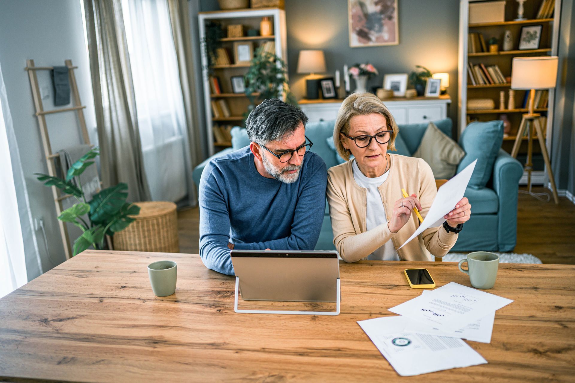 An elderly couple is sitting at a table looking at papers and a tablet.