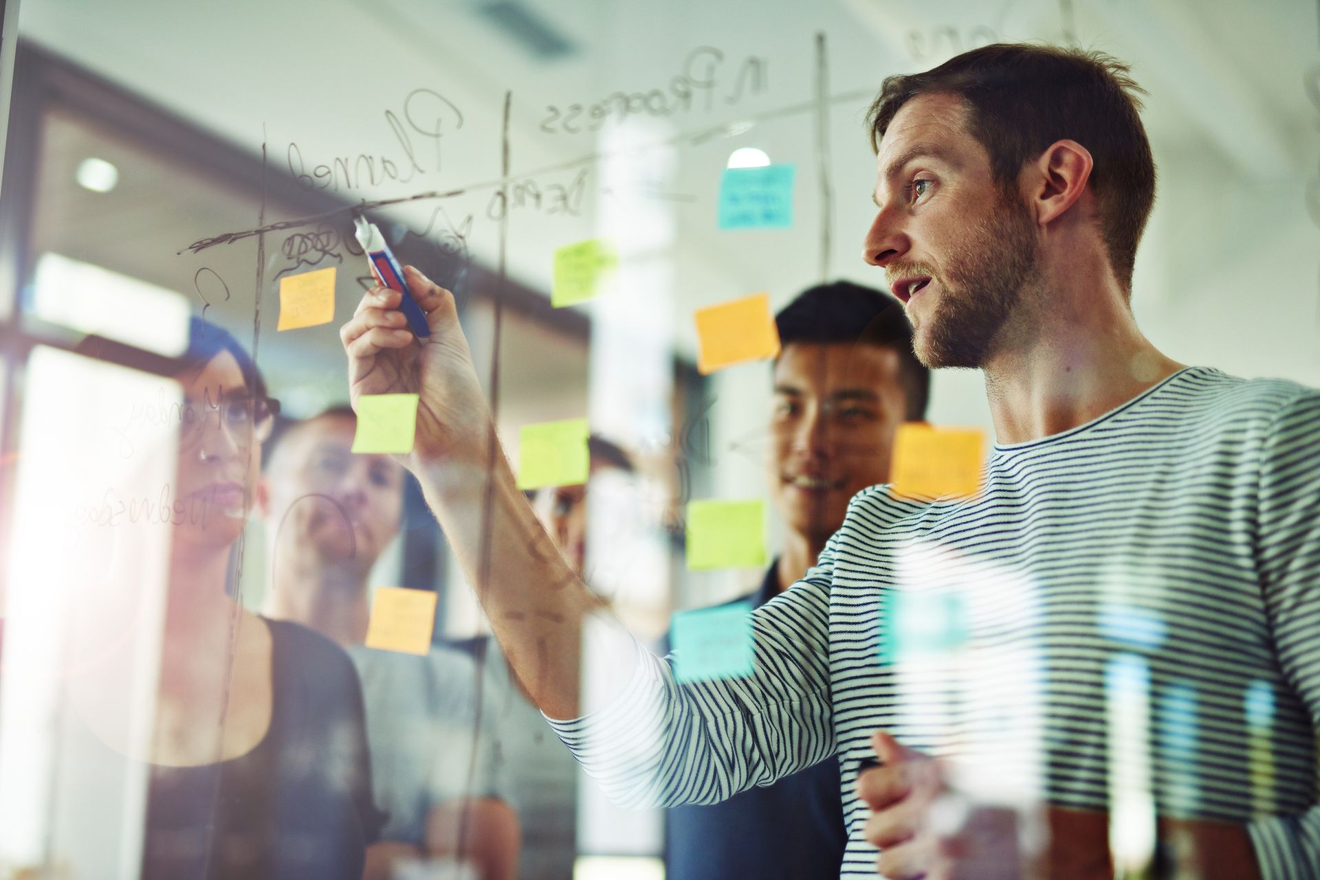 A group of people are looking at sticky notes on a glass wall.