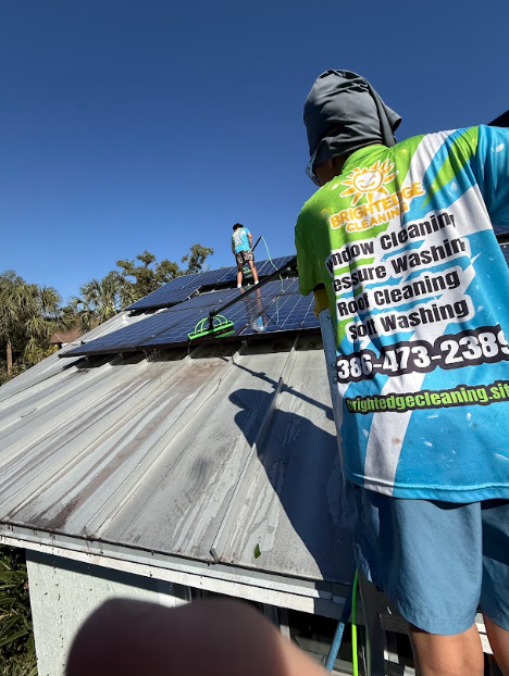 Two people cleaning solar panels on a rooftop; one is wearing a cleaning company shirt.