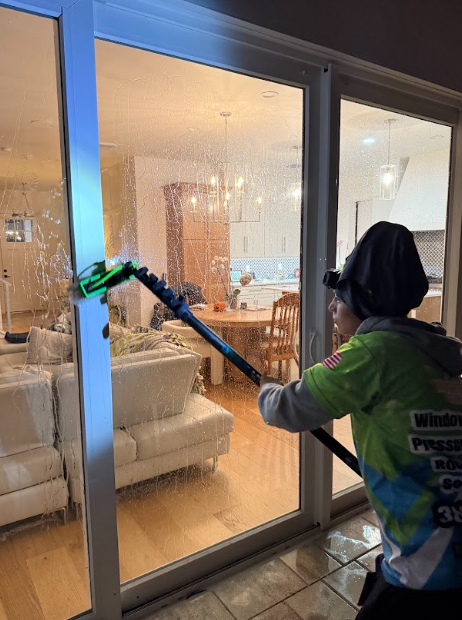 Person cleaning a sliding glass door with an extended cleaning tool.