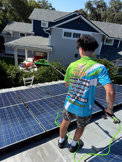 Person cleaning solar panels on a roof, wearing a company shirt.