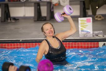 A woman is lifting a purple dumbbell in a swimming pool.