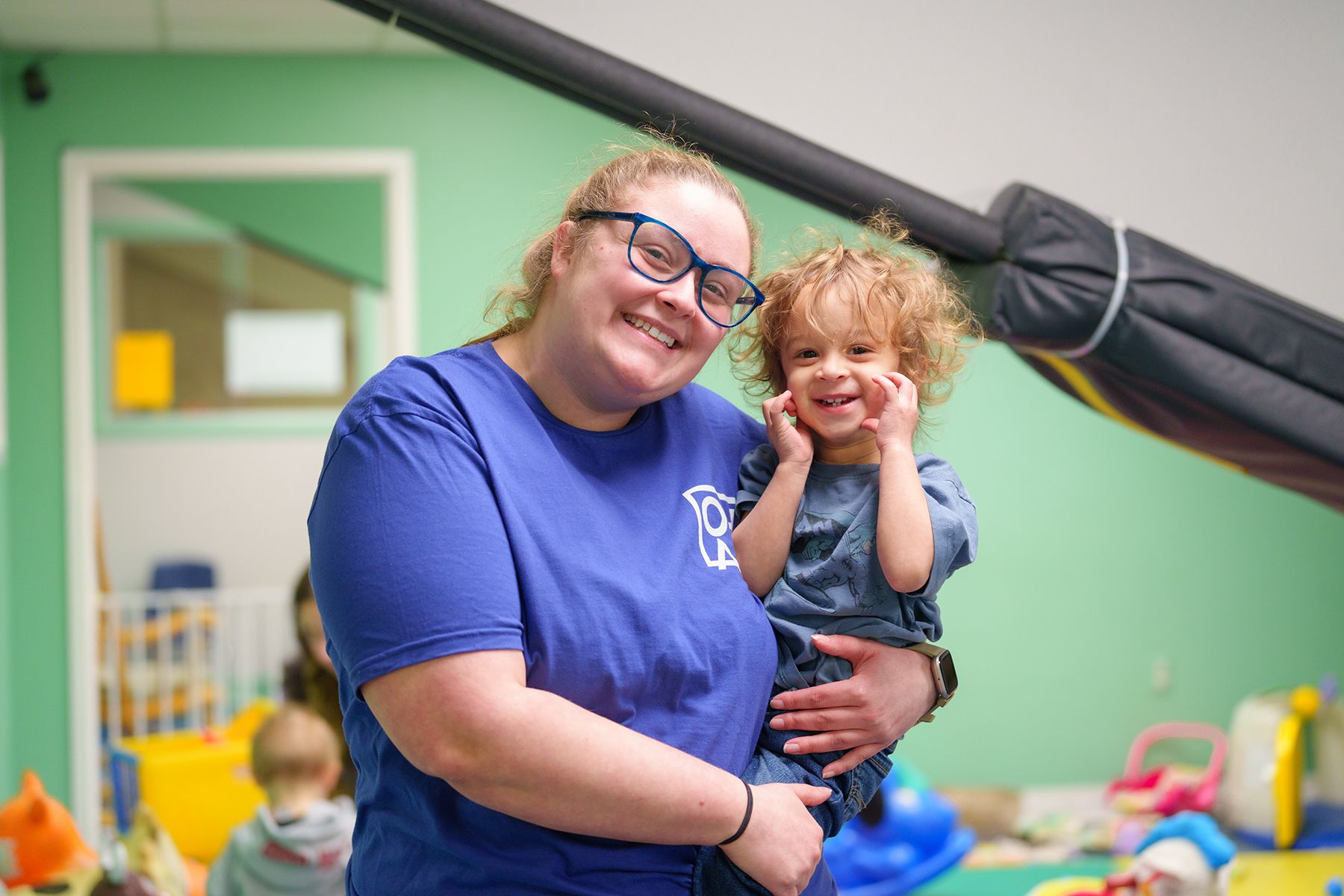 A woman in a blue shirt is holding a little boy in her arms.