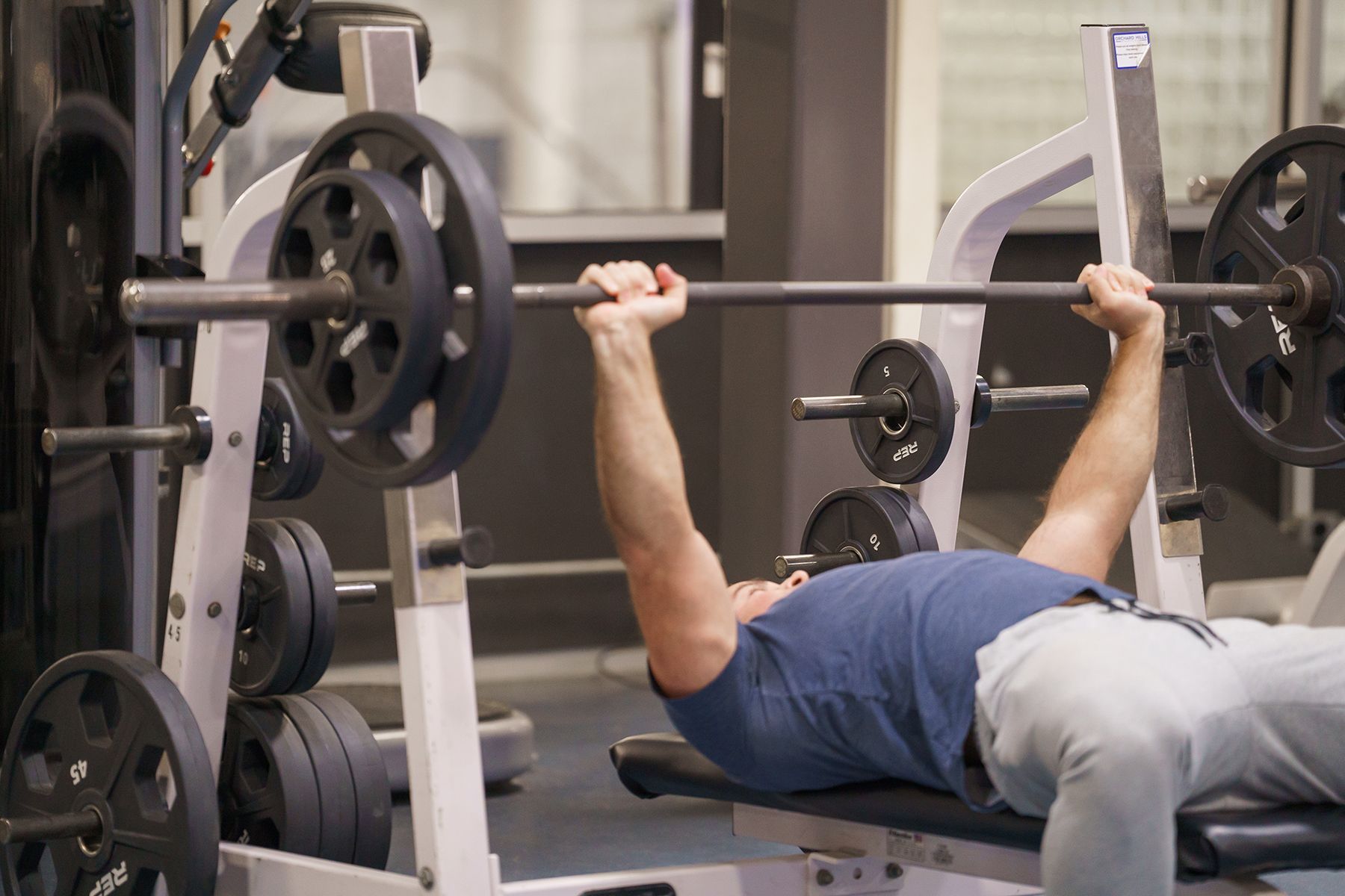 A man is laying on a bench lifting a barbell in a gym.