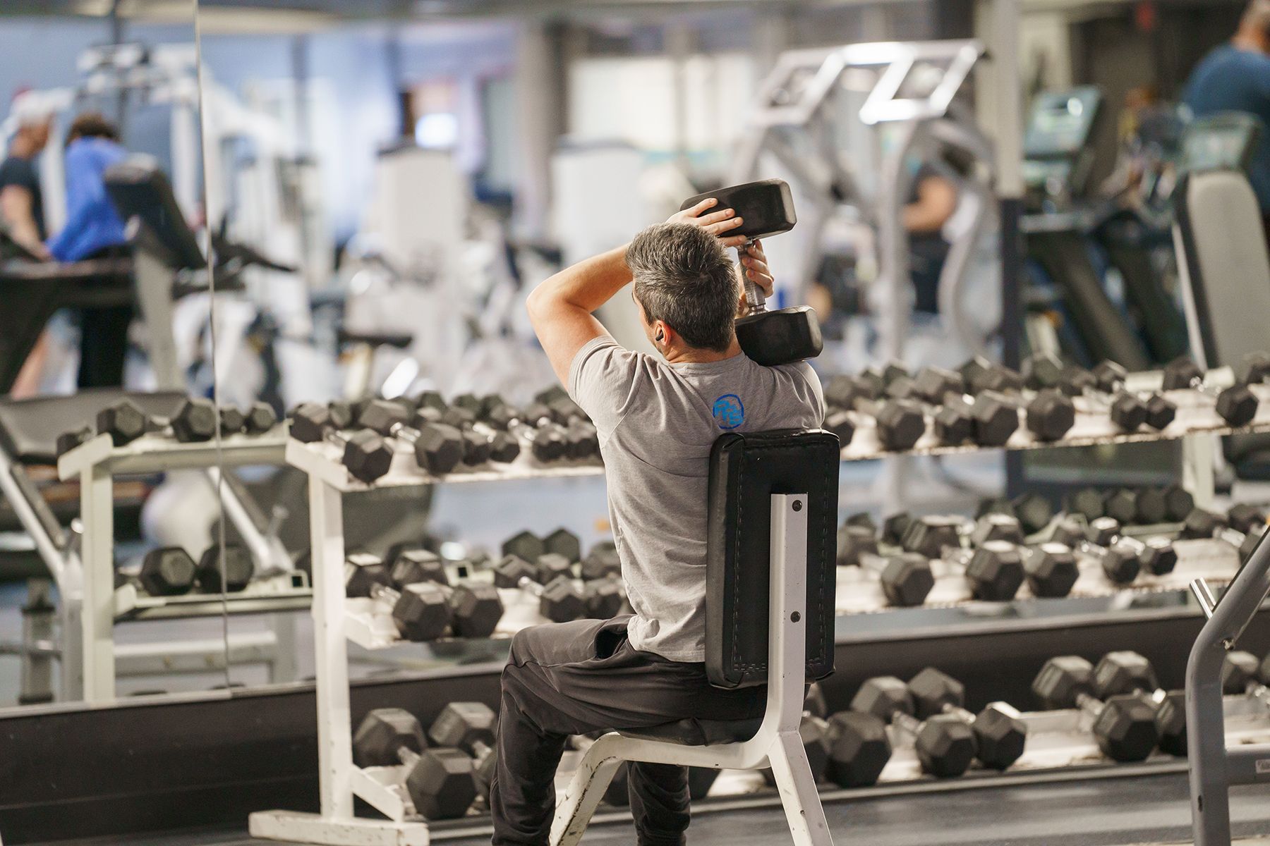 A man is sitting on a bench in a gym holding a dumbbell.