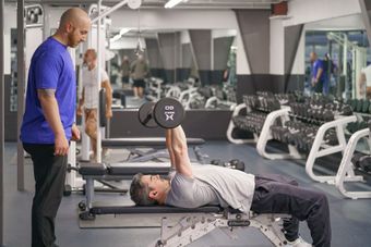 A man is lifting a dumbbell while laying on a bench in a gym.