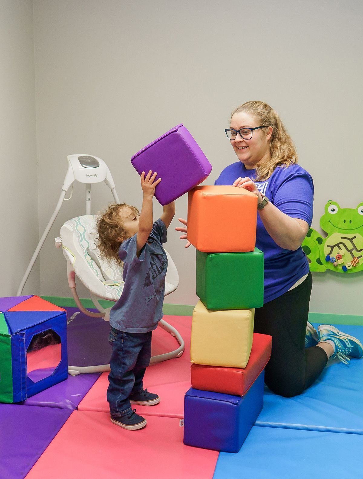 A woman and a child are playing with blocks in a play room.