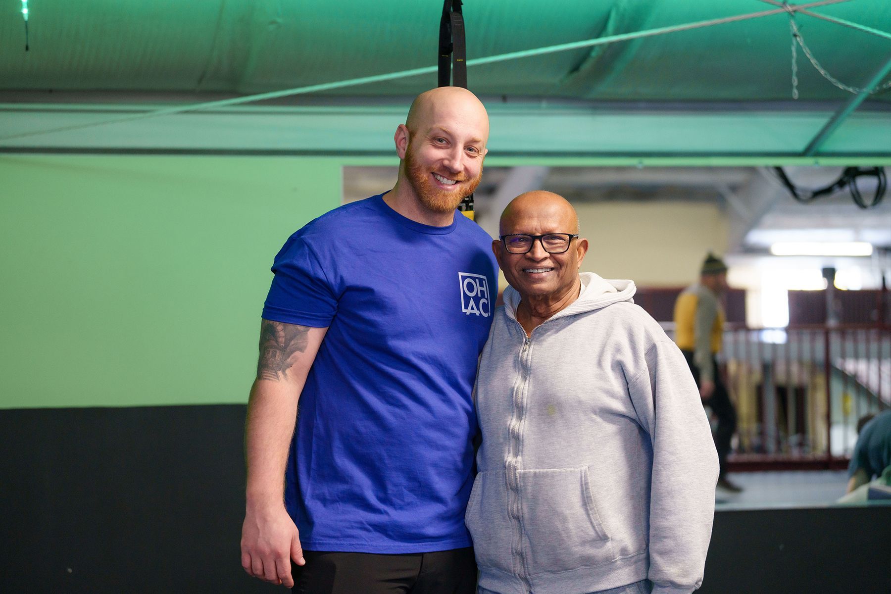 Two men are posing for a picture in a gym.