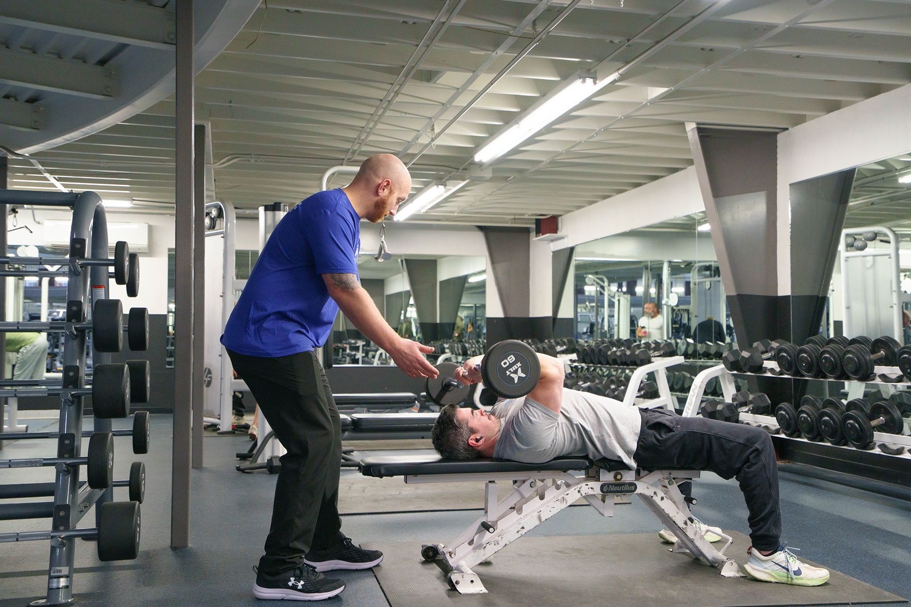 A man is lifting a dumbbell on a bench in a gym.