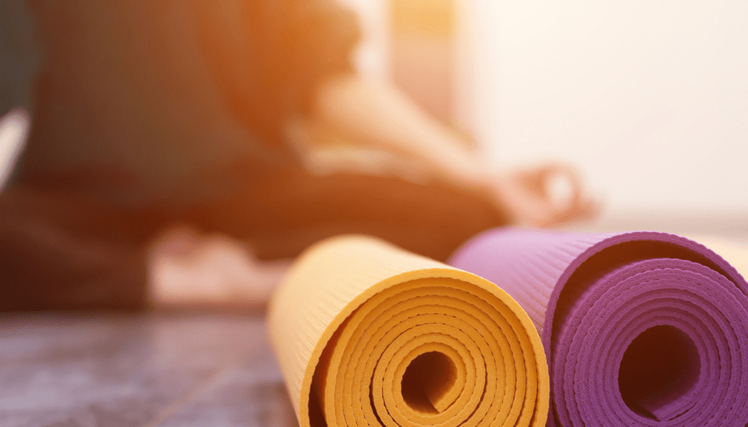 A person is sitting on the floor next to three yoga mats.