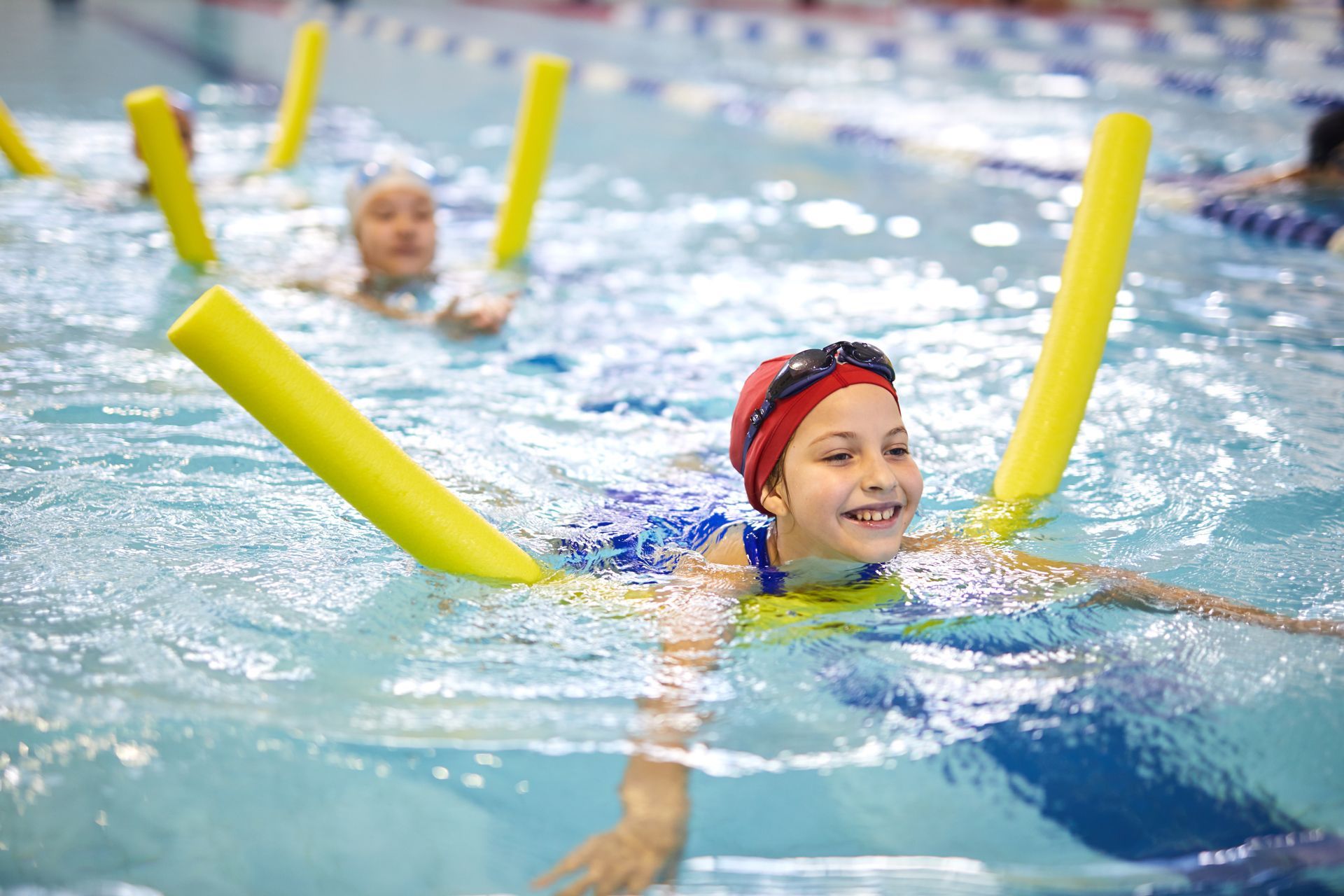 A group of children are swimming in a swimming pool with foam noodles.