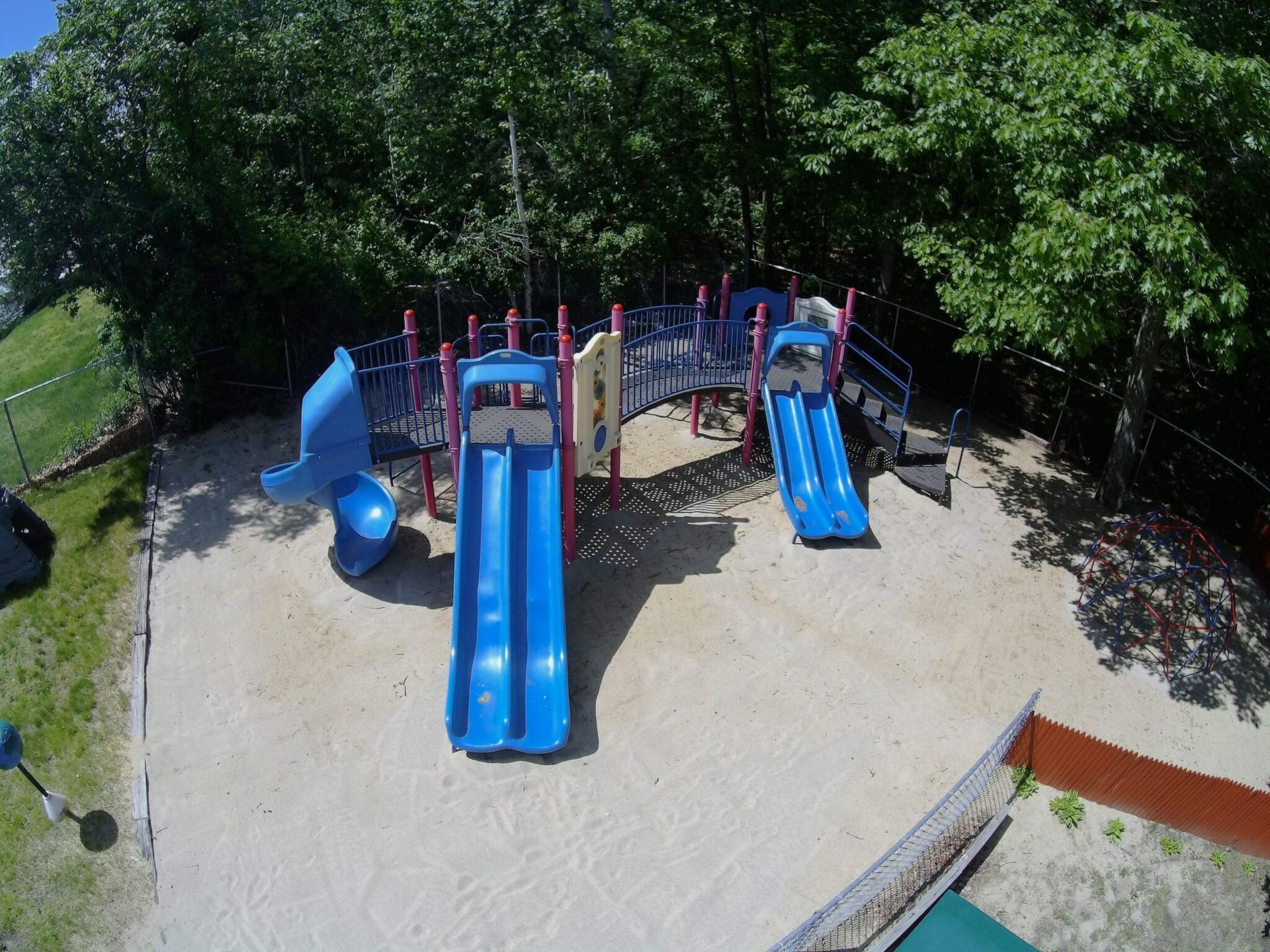 An aerial view of a playground with blue slides surrounded by trees.