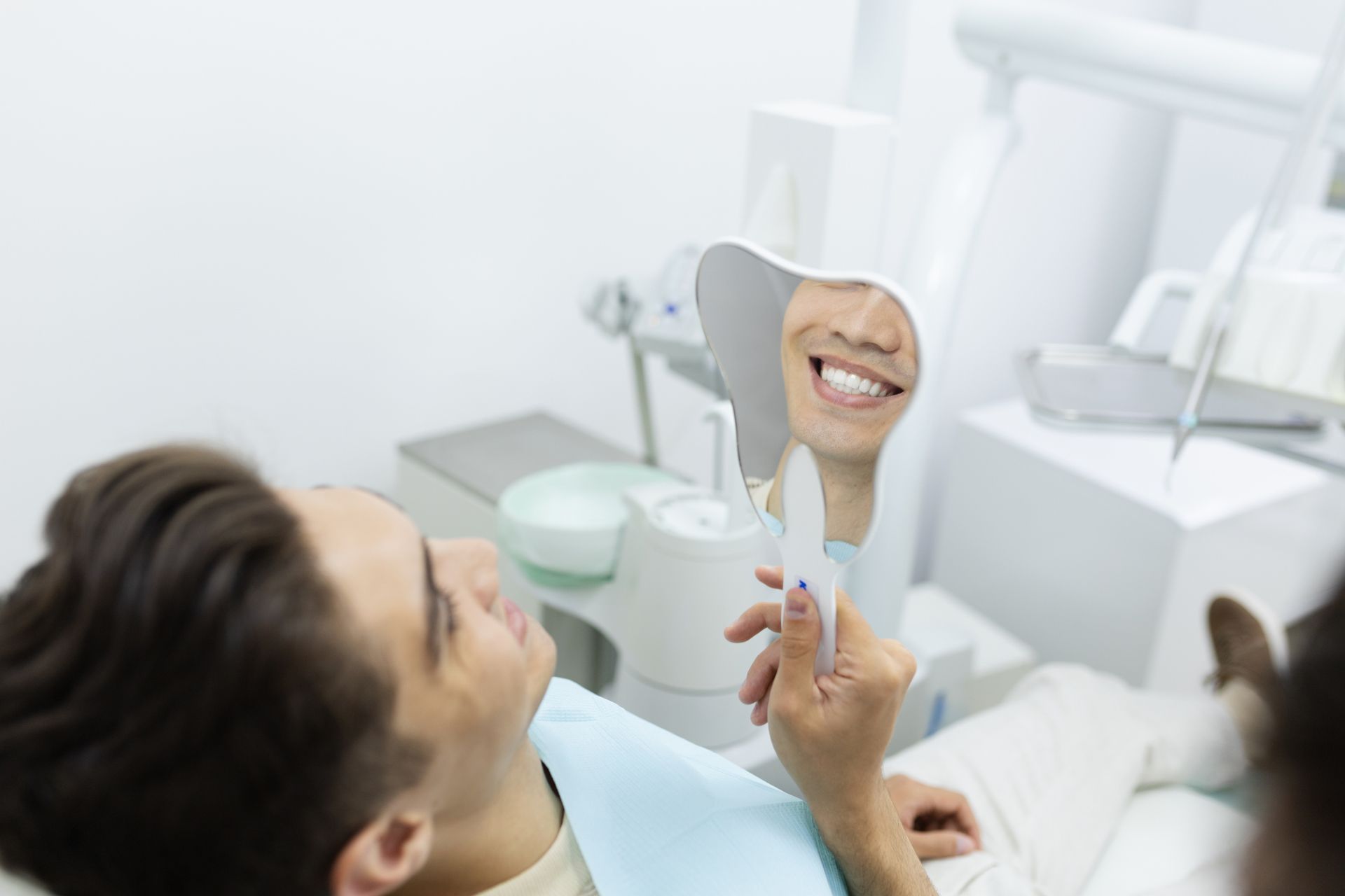 A man is sitting in a dental chair looking at his teeth in a mirror.