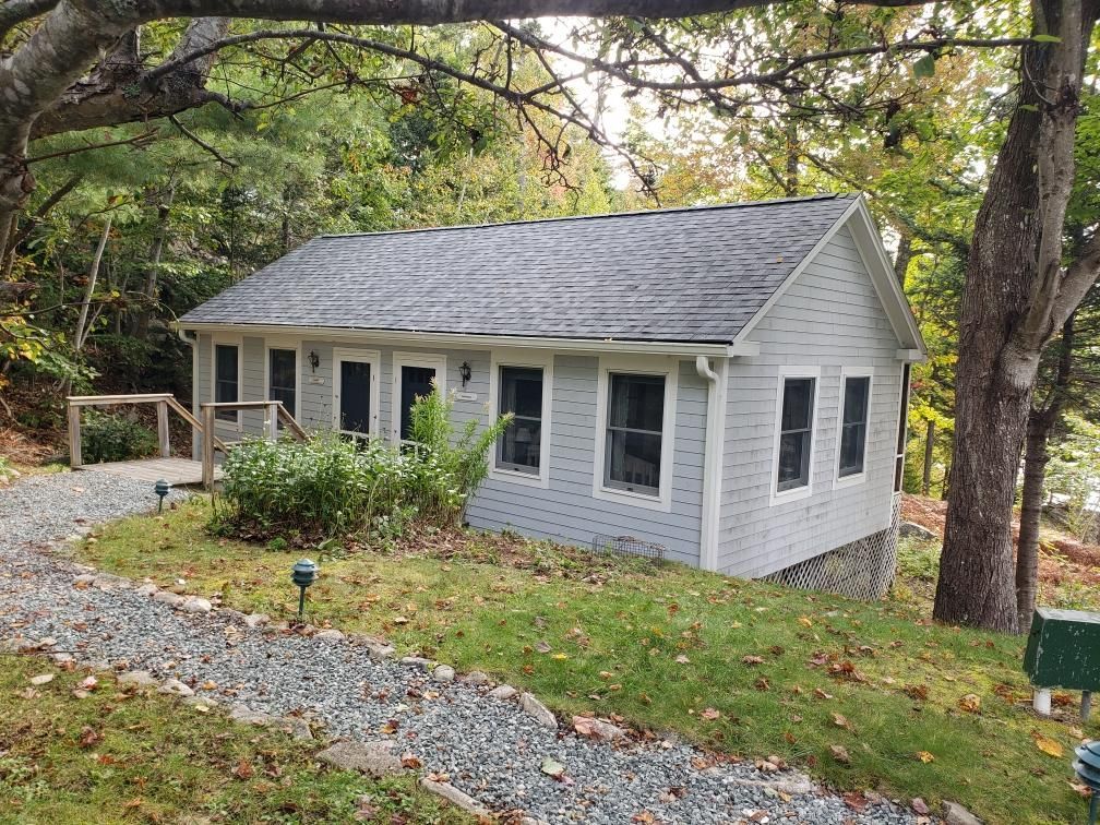 A small white house is sitting on top of a grassy hill surrounded by trees.