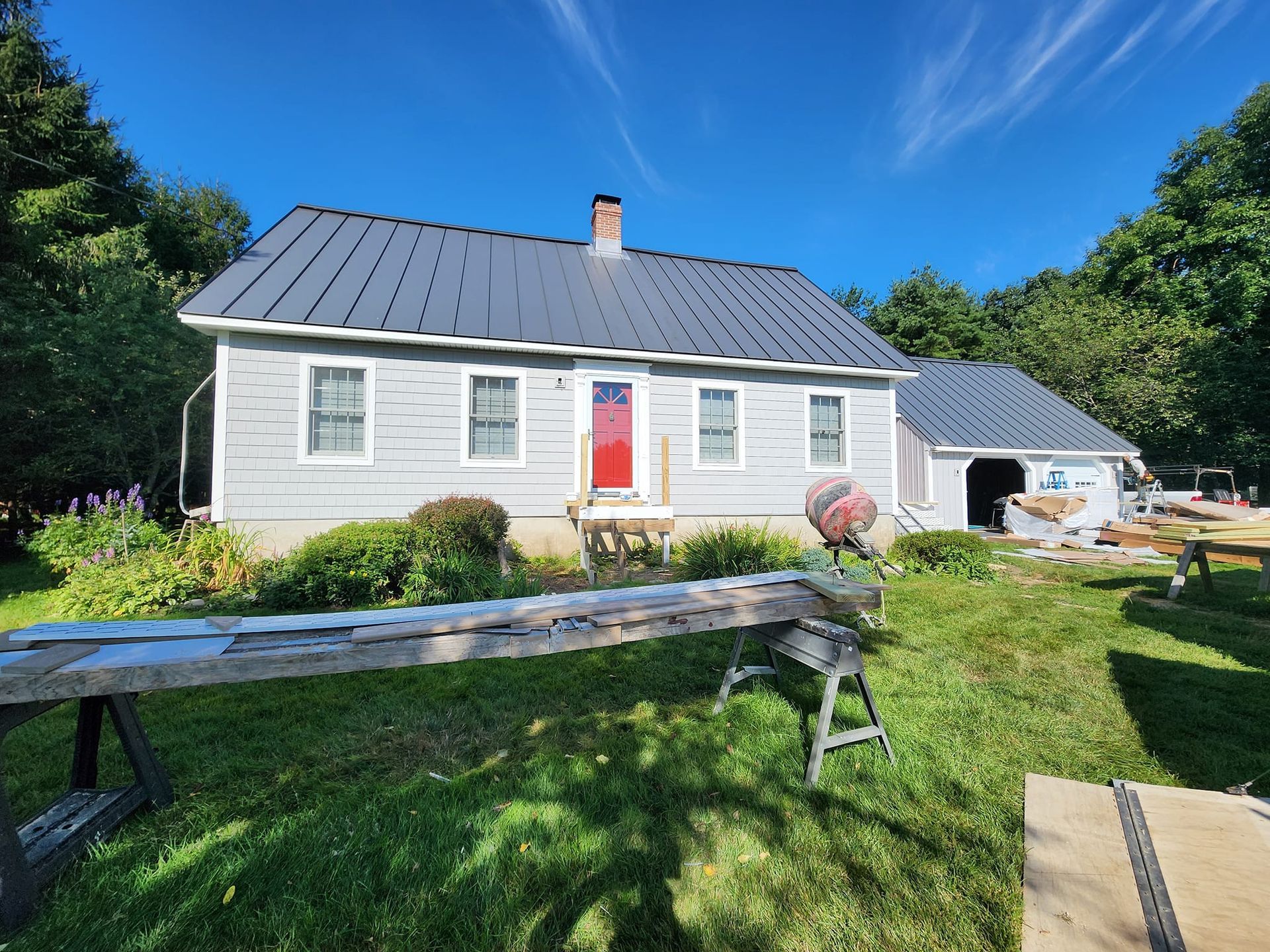 A white house with a black roof and a red door is being remodeled.