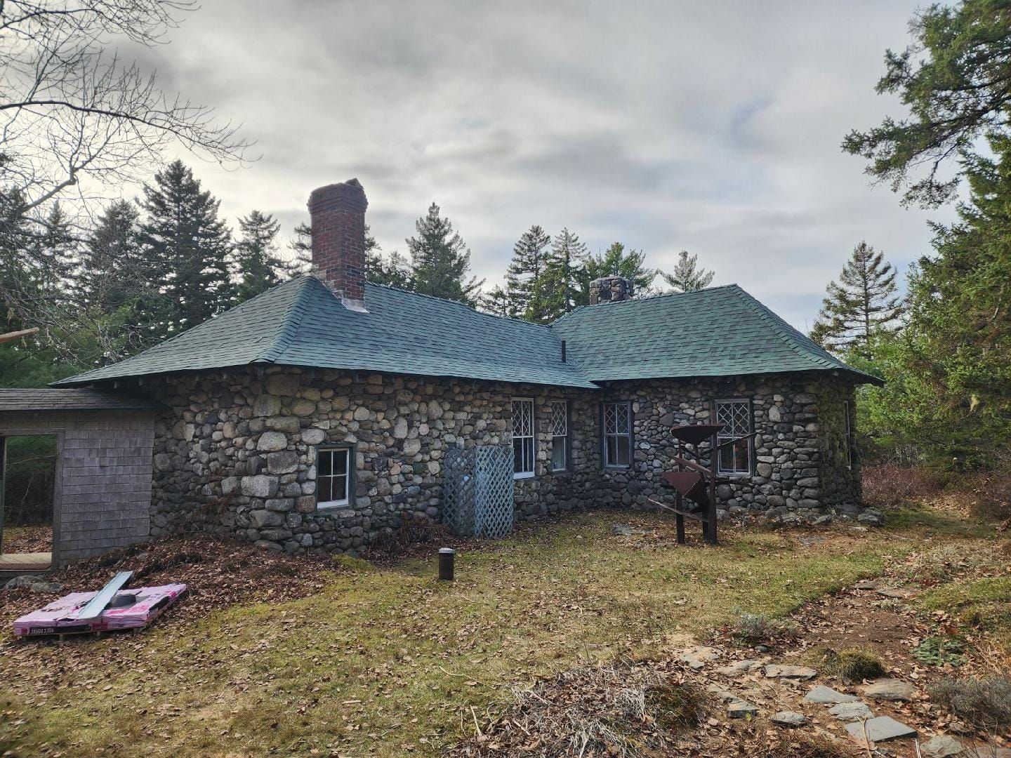 A stone house with a green roof is surrounded by trees