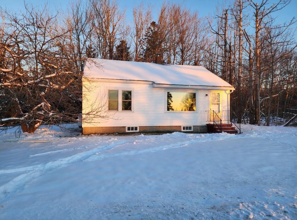 A small white house is surrounded by snow and trees.