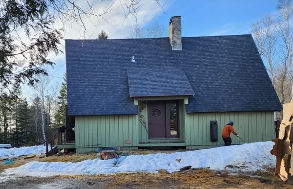 A man is standing in front of a green house with a black roof.