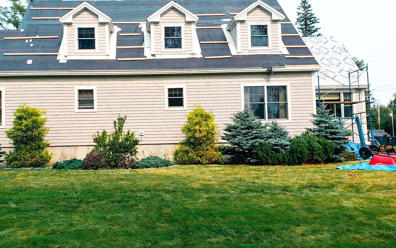 A house with a roof that is being installed is sitting on top of a lush green lawn.