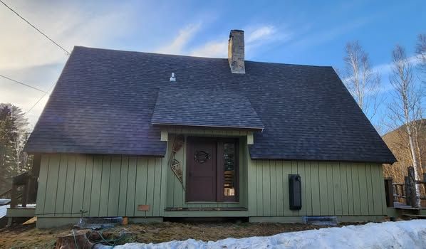 A green house with a black roof and a chimney in the snow.