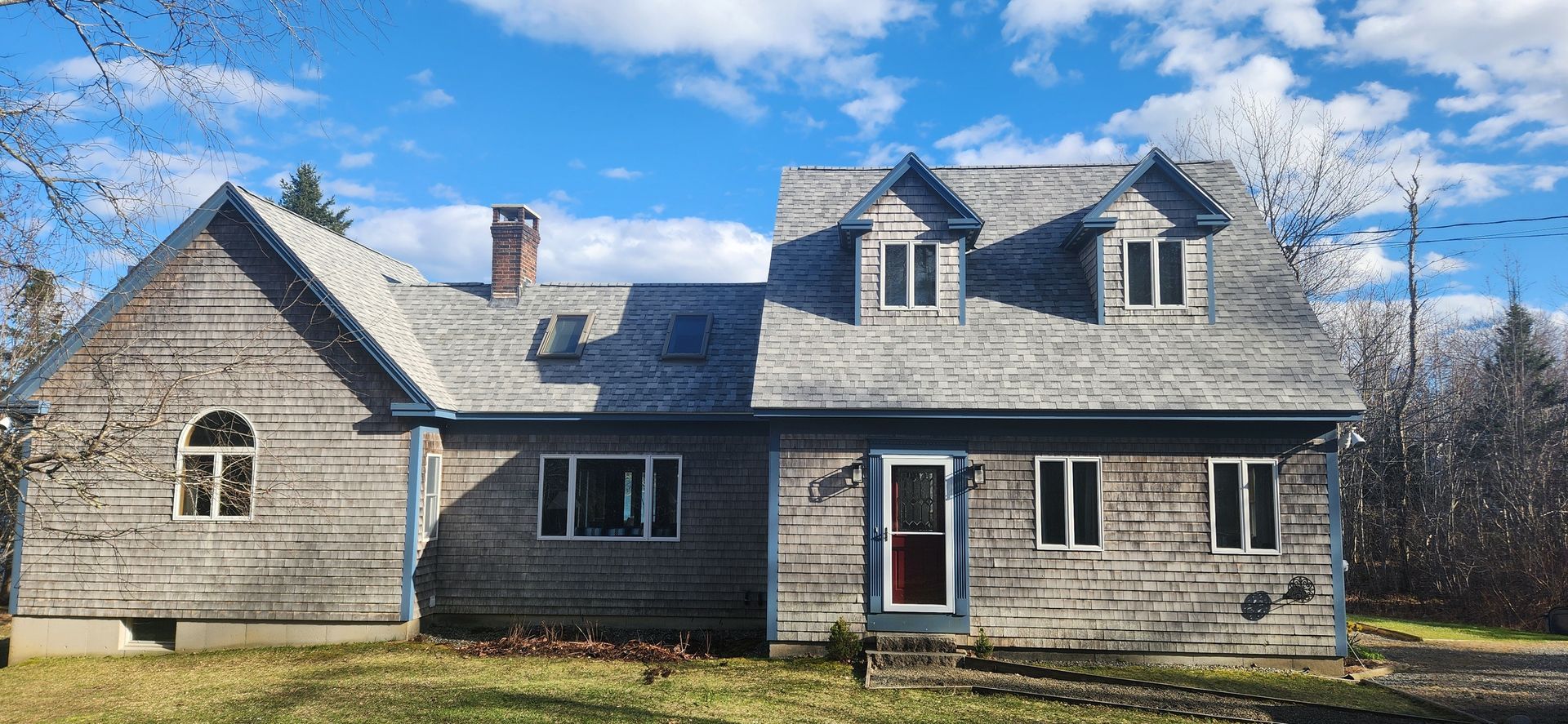 A large wooden house with a gray roof is sitting on top of a lush green field.