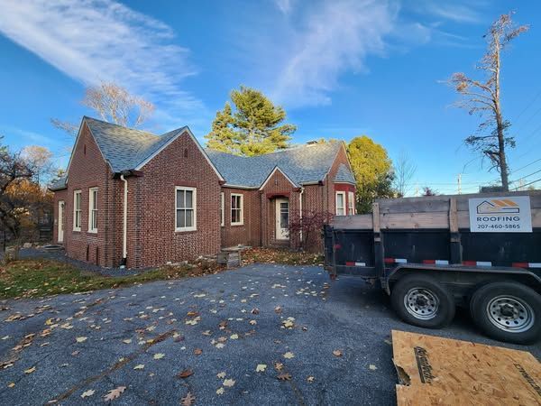 A dumpster is parked in front of a brick house.