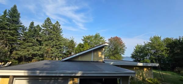 A house with a black roof and trees in the background.