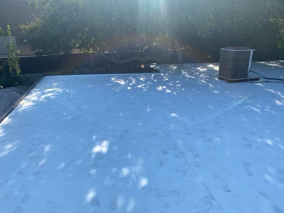 A white roof with a fan on top of it and trees in the background.