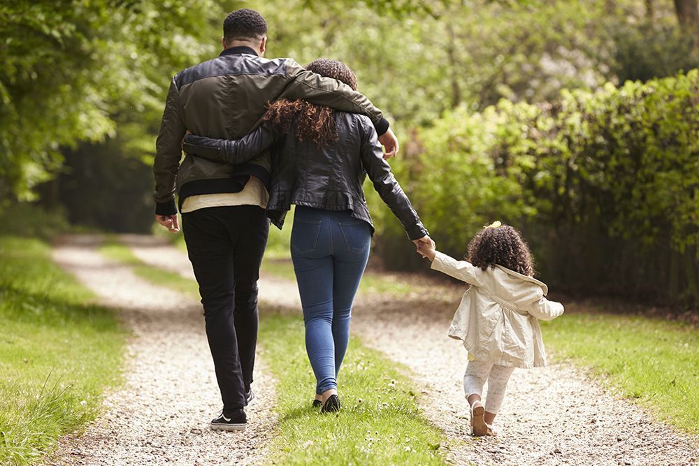 Three people walking hand in hand on a gravel path through a green park