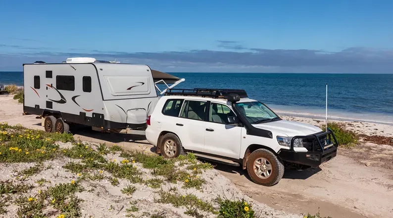 A White 4WD Towing A Caravan On A Beach Road — Brake & Clutch Automotive Services in Ciccone, NT