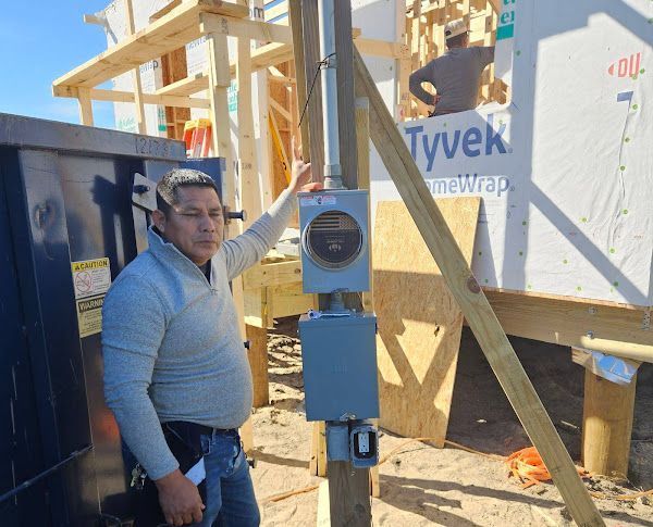 Man points to electrical meter on a pole near a construction site.