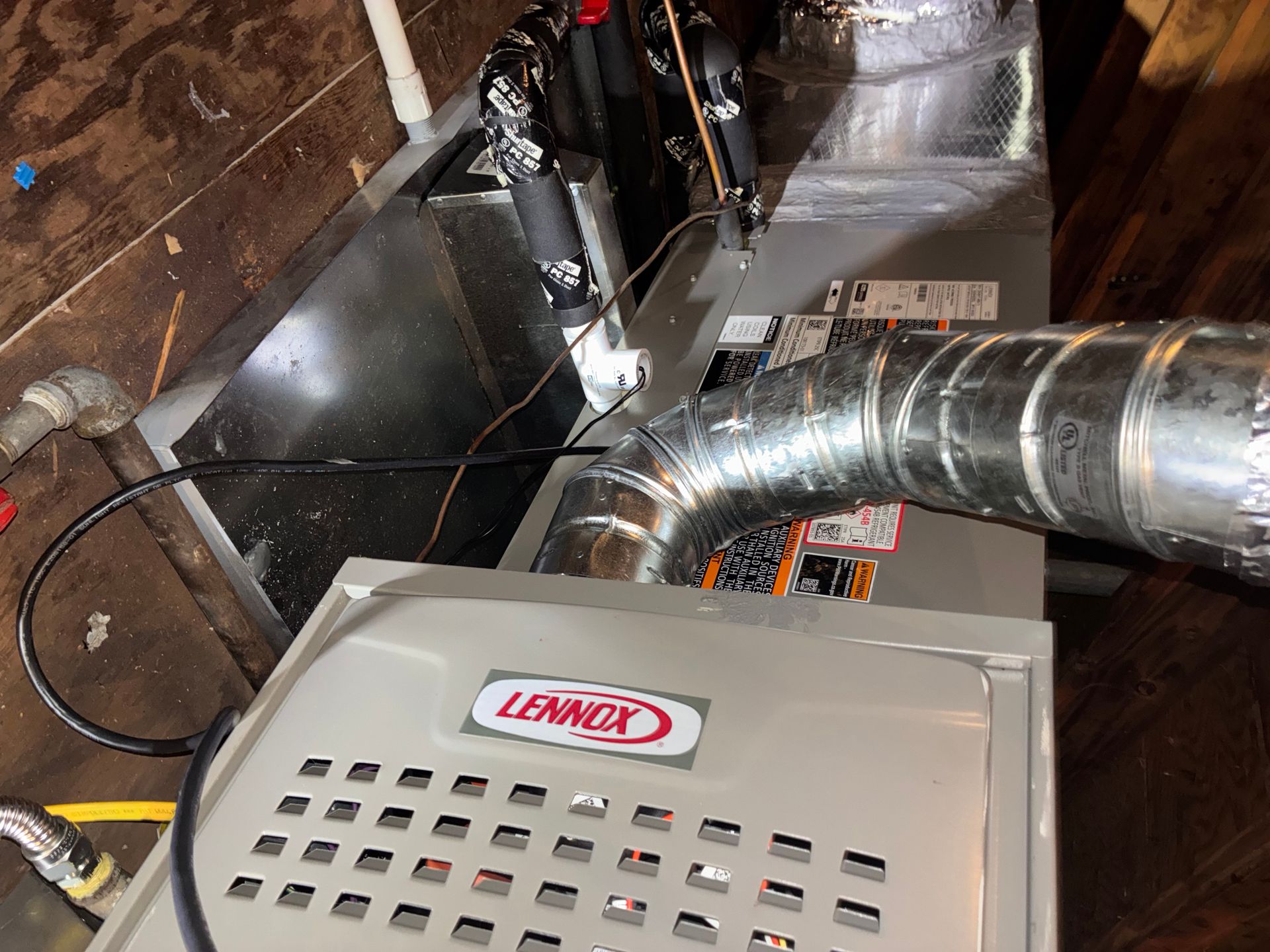 Lennox HVAC unit in attic, silver ductwork, gray metal base, dark wiring, wooden floor.