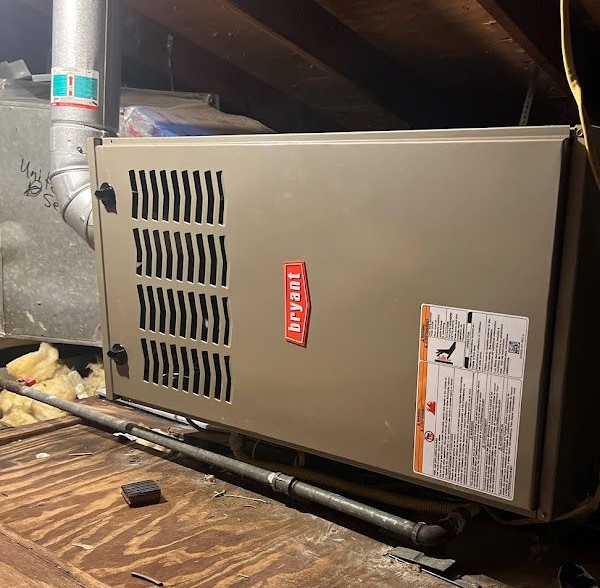 Bryant furnace in an attic. Beige metal casing with a red logo. Silver exhaust pipe.