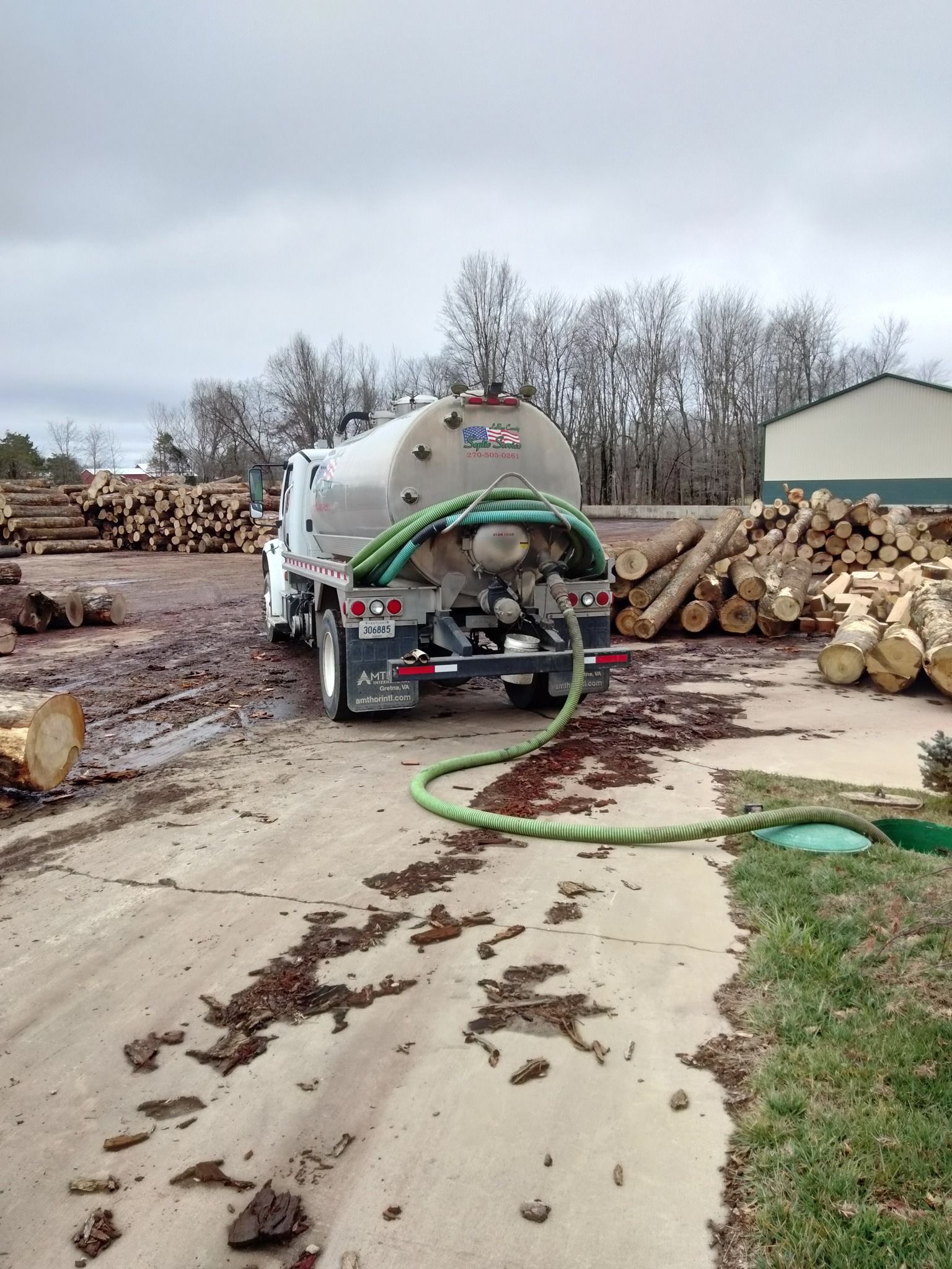 a tanker truck is driving down a dirt road next to a pile of logs .