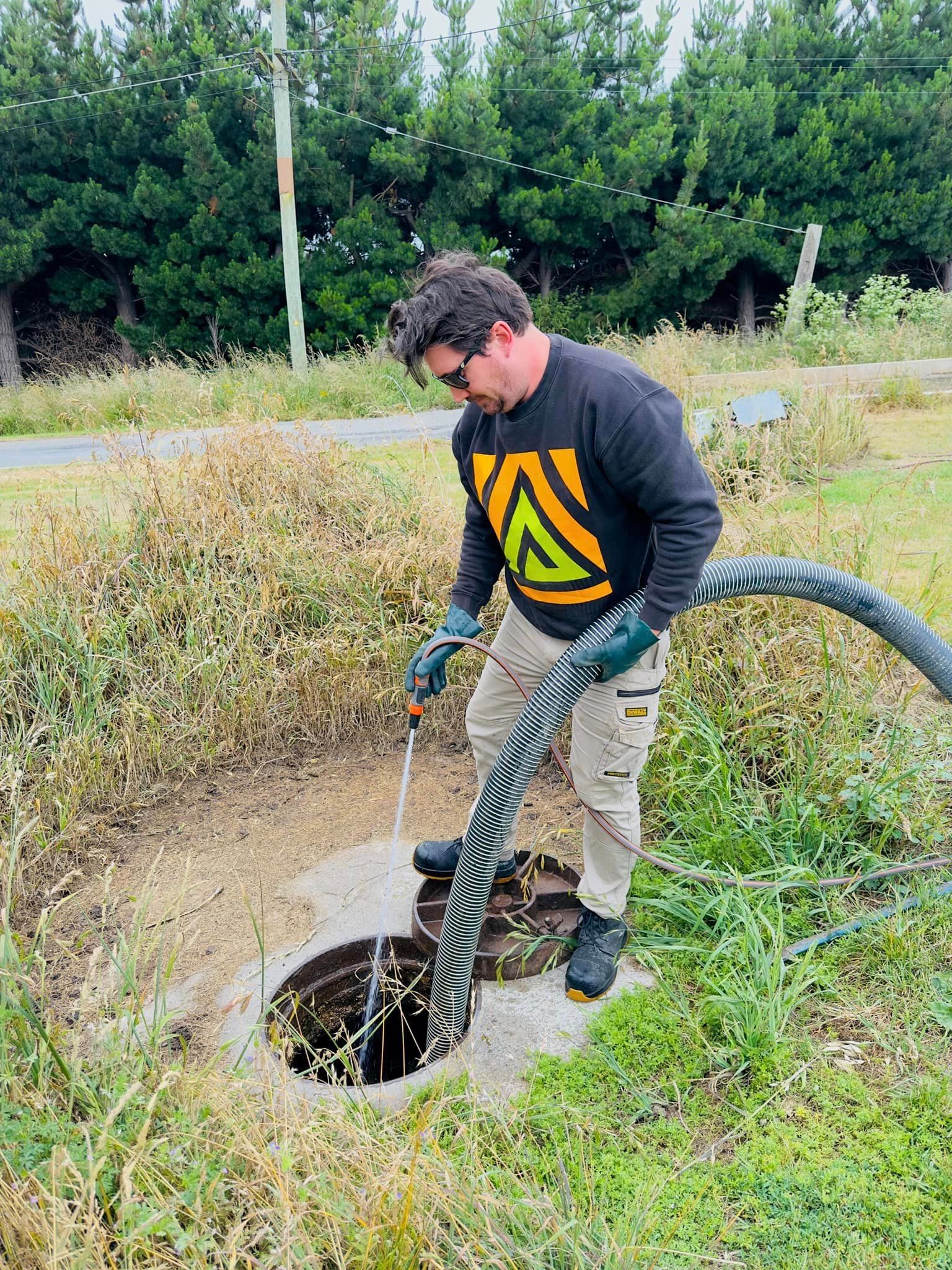 a man is pumping water into a manhole cover with a hose .