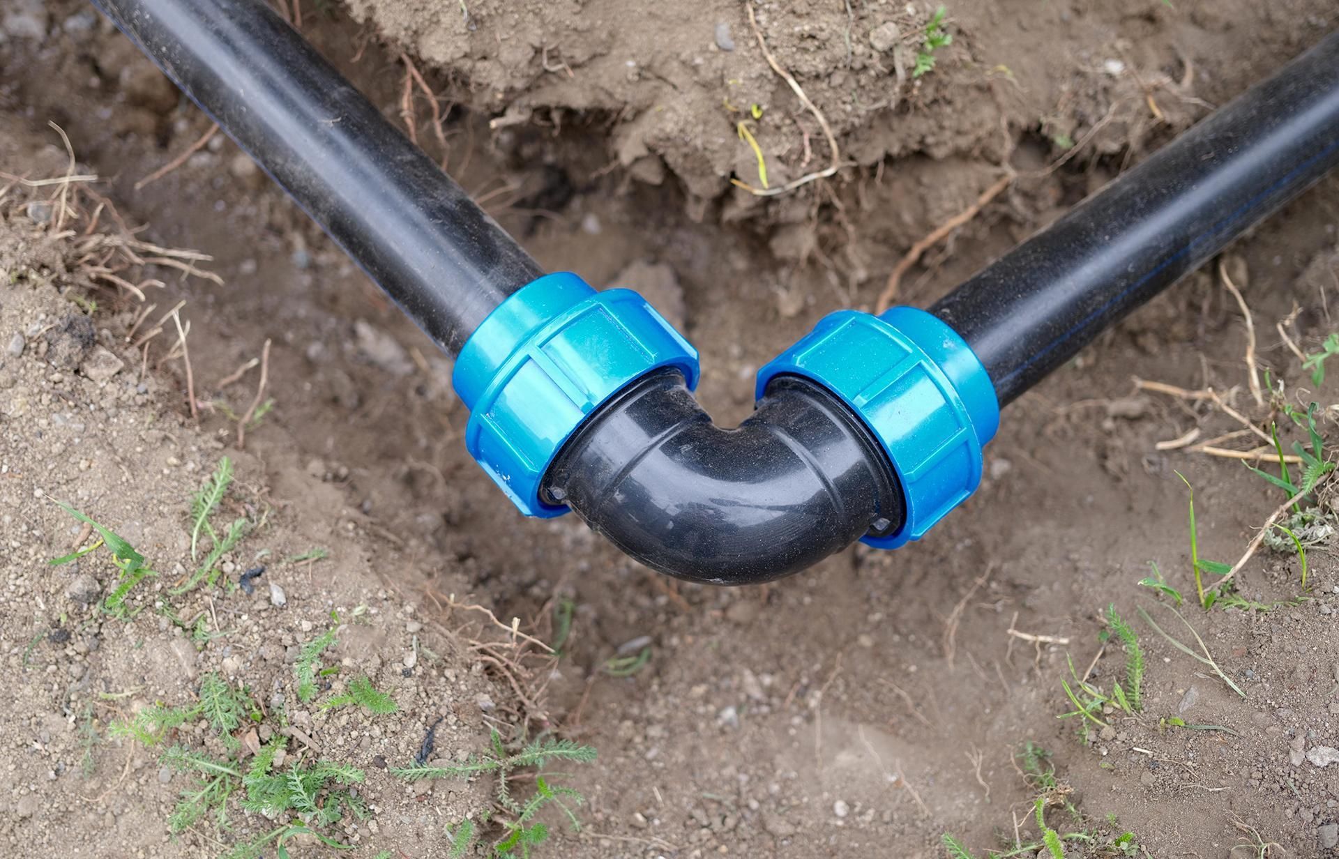 two black pipes with blue connectors are connected to each other in the dirt .