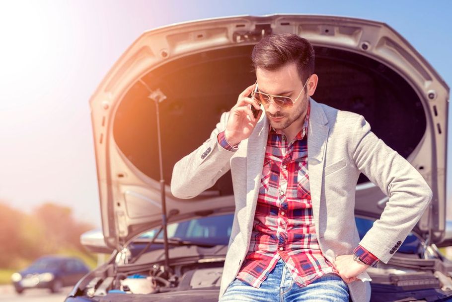 Man on phone next to broken down car with hood open.