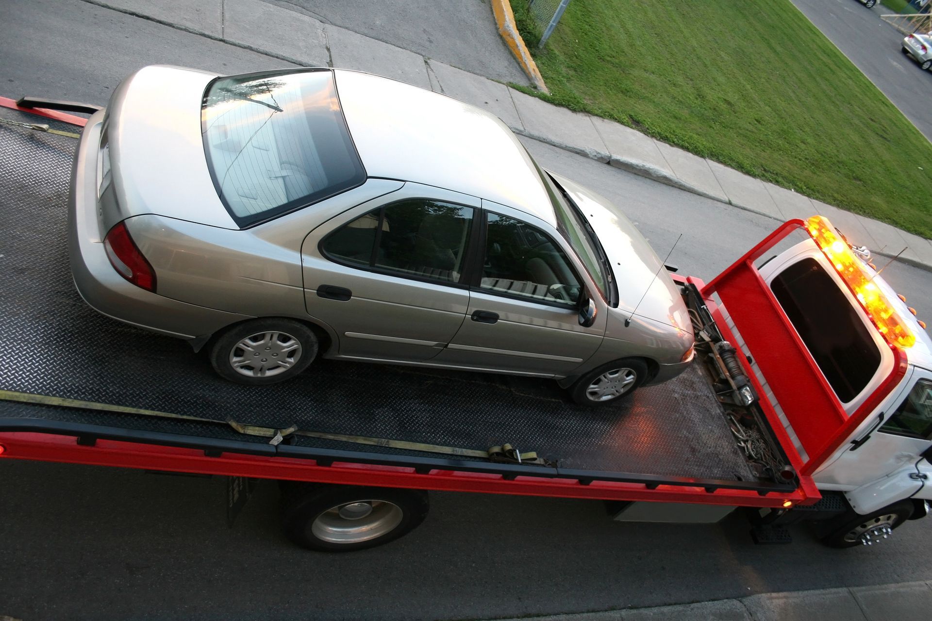 Overhead view of a silver car secured on a flatbed tow truck.