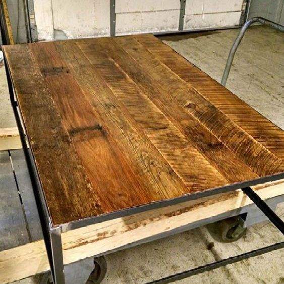 A reclaimed wooden table with a metal frame is sitting on a cart.