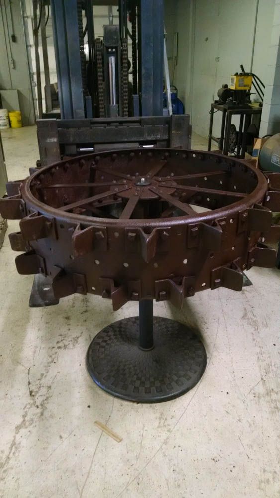 A table made out of a tractor wheel is sitting in a room next to a forklift.