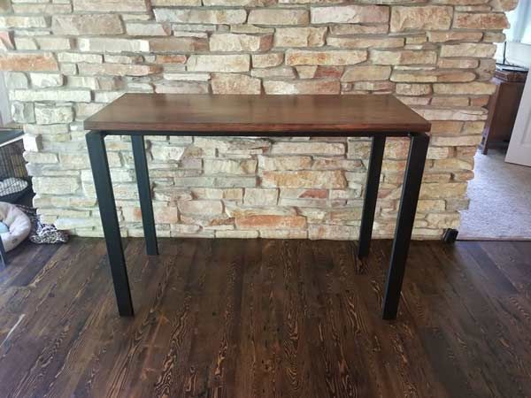 A tailor made wooden table with metal legs is sitting in front of a brick wall.