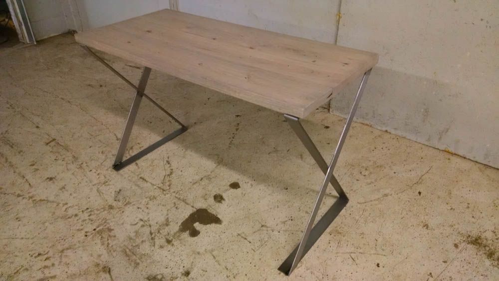 A wooden table with metal legs is sitting on a dirty floor.