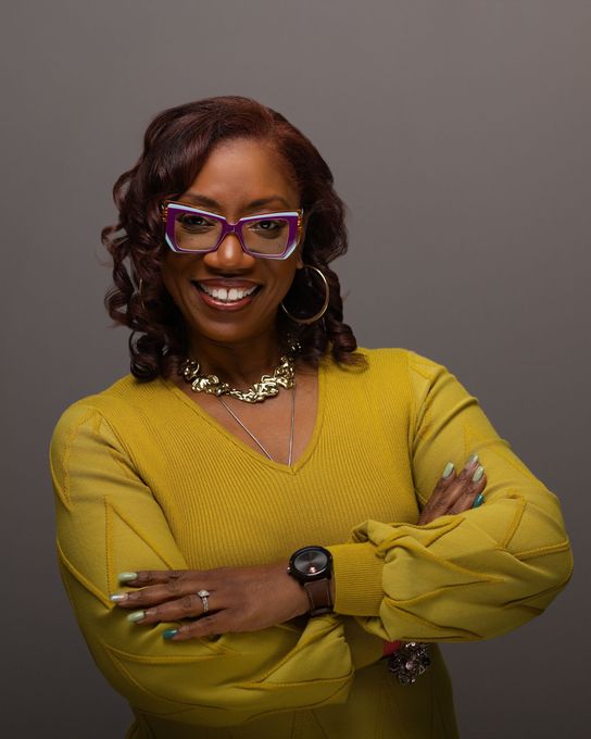 A woman is sitting at a desk with a laptop and a vase of flowers.