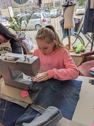 Meisje in een roze trui gebruikt een naaimachine om een ​​spijkerbroek te repareren in een winkel.