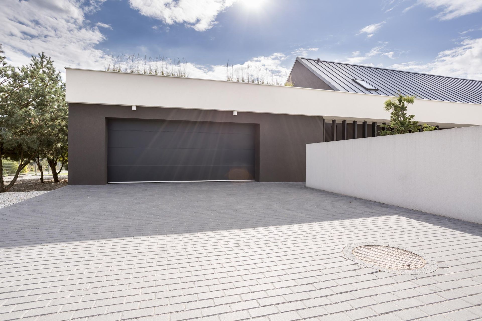 Garage with gray door and white walls, light gray brick driveway, blue sky.
