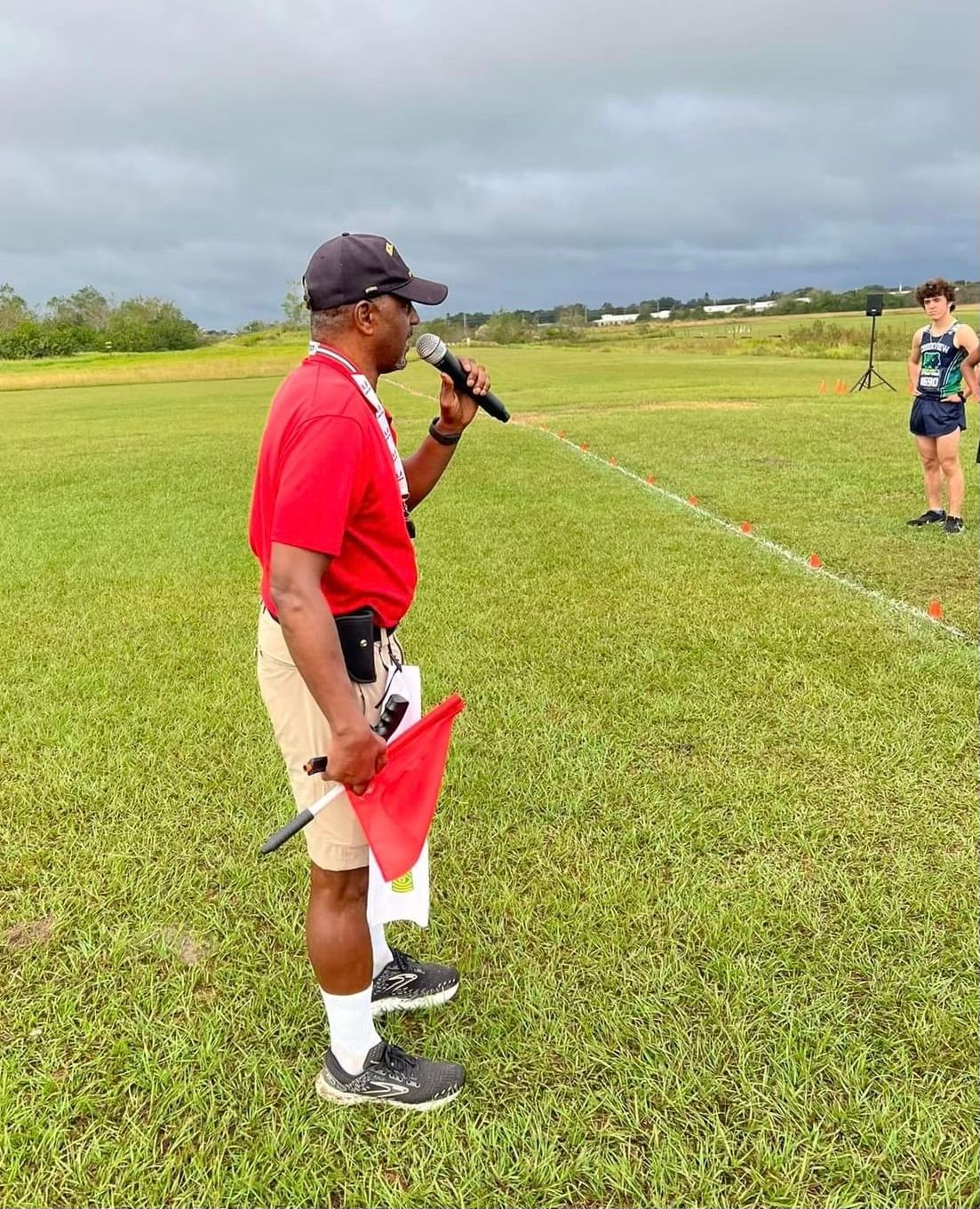 A man is standing in a field holding a microphone and a red flag.