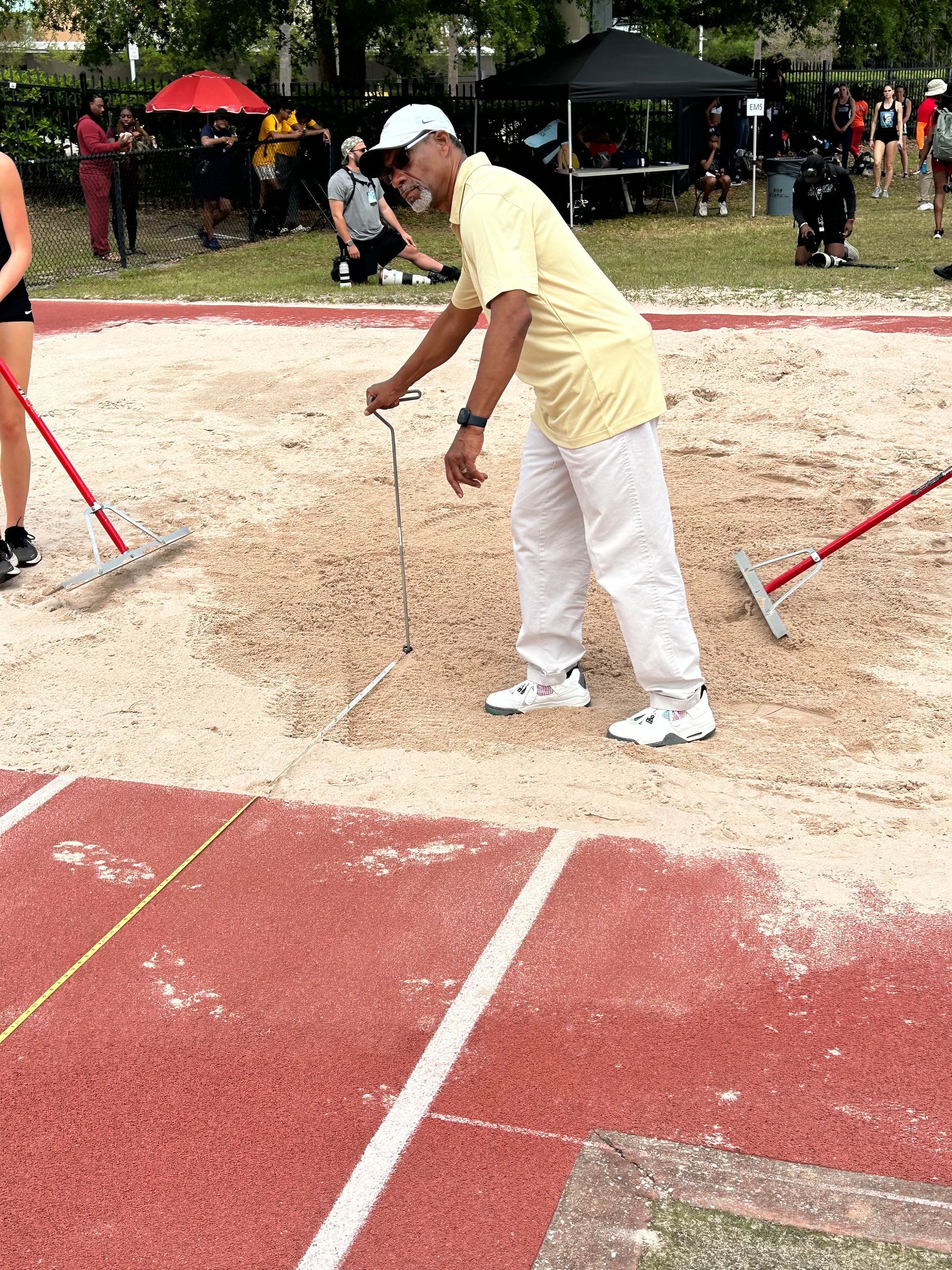 A man is raking dirt on a track with a rake.